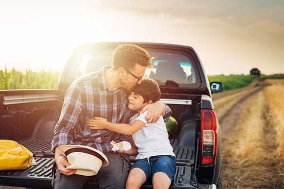 Farmer in a wheat field outside Carrington, ND, eating lunch in the bed of his pick-up with his young son