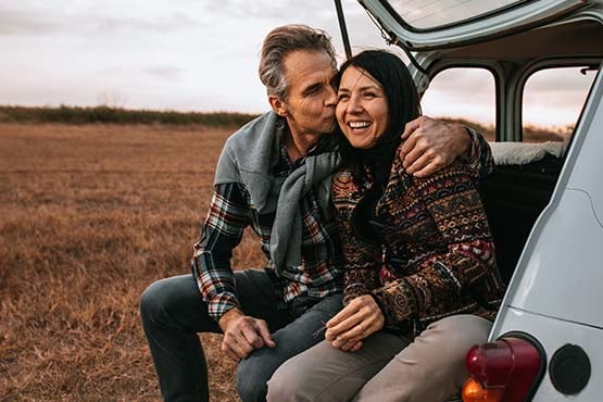 Happy fortysomething couple enjoying an autumn sunset, sitting in the back of a car on a dirt road outside of Williston, ND