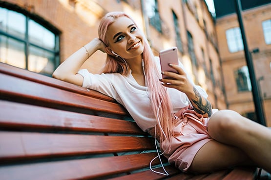 Young smiling woman with long pink hair, ordering a custom debit card from Gate City Bank on her phone in downtown Fargo, ND