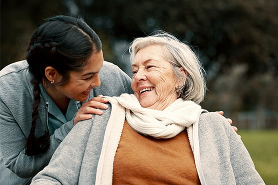 A young woman and a female senior citizen exchange smiles in a park after learning tips to fight elder financial abuse